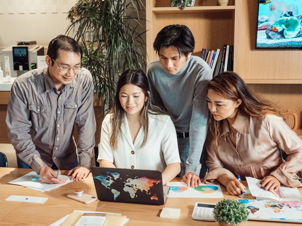 Photo by Kindel Media A diverse group of professionals collaborating over a laptop in a modern office setting.