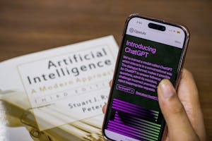Close-up of a smartphone displaying ChatGPT app held over AI textbook. Close-up of a smartphone displaying ChatGPT app held over AI textbook.