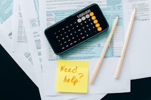 Top view of financial papers with a calculator, pencils, and a note saying 'Need help?' indicating tax or accounting assistance. Top view of financial papers with a calculator, pencils, and a note saying 'Need help?' indicating tax or accounting assistance.