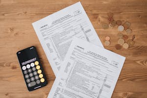 Top view of tax documents, calculator, and coins on wooden table. Top view of tax documents, calculator, and coins on wooden table.